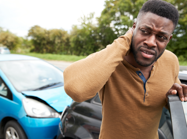 a man holding his neck indicating a soft tissue injury, with a rear-end car accident behind him