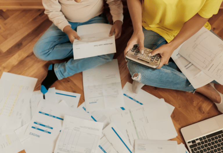 overhead view of two people sitting on the floor and one is holding a calculator as they review papers on the floor