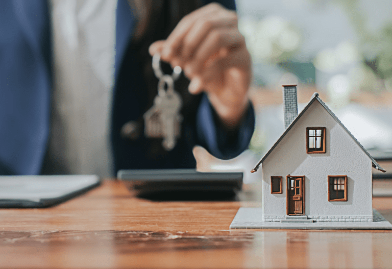 man holding keys in the background of a small white model house