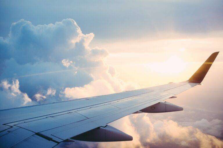 view of an airplane wing in the flight with clouds and sunset in the background