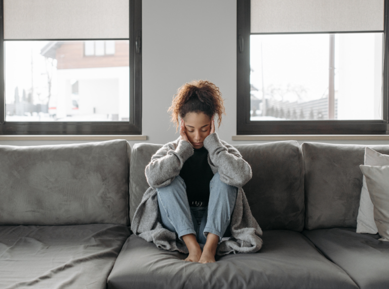 a woman on a couch holding her head indicating head pain