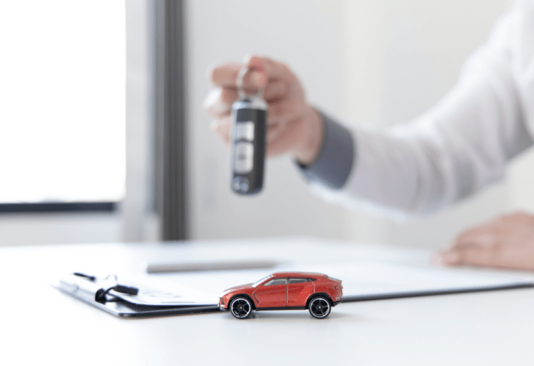 a person holding car keys over a clipboard with a small red toy car in the foreground